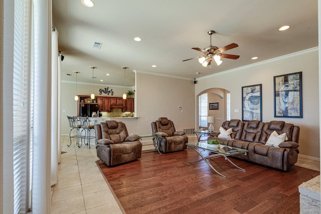 living room with light wood-type flooring, recessed lighting, arched walkways, and ornamental molding