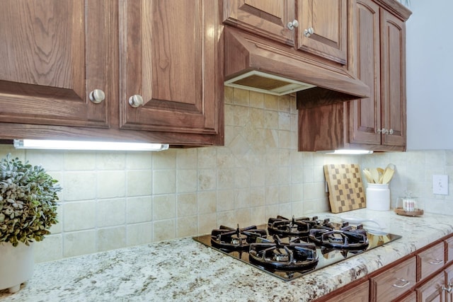 kitchen featuring custom exhaust hood, light stone counters, black gas cooktop, and tasteful backsplash