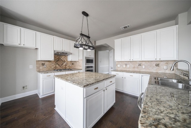 kitchen with a sink, stainless steel appliances, white cabinets, under cabinet range hood, and a center island