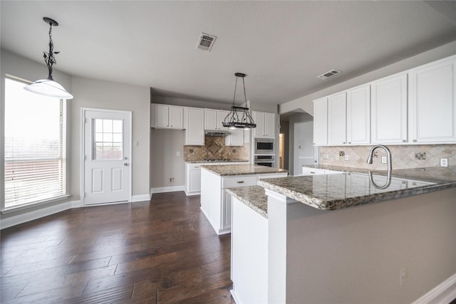 kitchen with a peninsula, light stone counters, visible vents, and stainless steel appliances