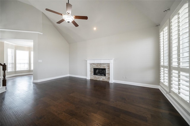 unfurnished living room with dark wood-type flooring, high vaulted ceiling, a ceiling fan, a stone fireplace, and baseboards