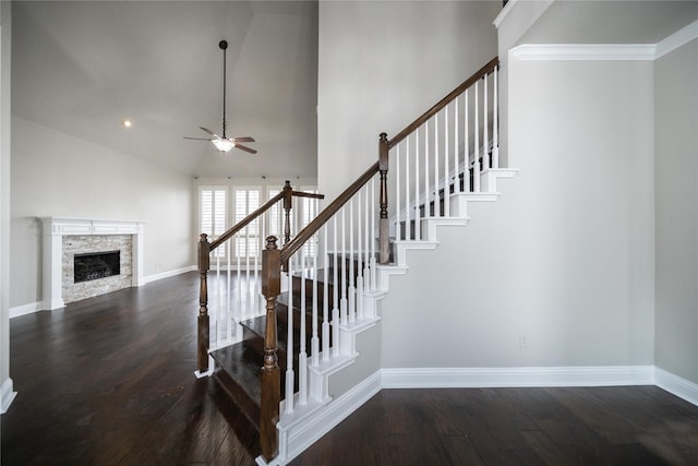 stairway with a fireplace, wood finished floors, baseboards, and ceiling fan