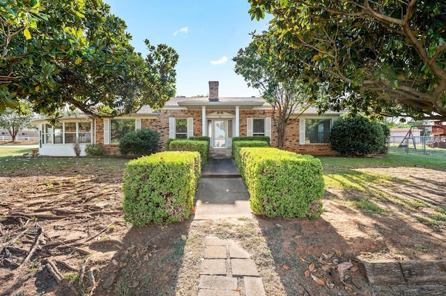 view of front facade featuring a front lawn, brick siding, a chimney, and fence