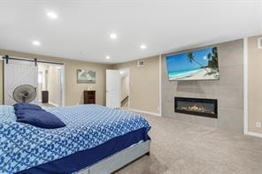 bedroom featuring a glass covered fireplace, recessed lighting, a barn door, carpet, and baseboards