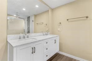 bathroom with a sink, wood finished floors, recessed lighting, double vanity, and baseboards