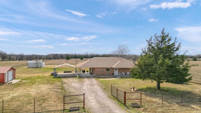 view of front of home with dirt driveway, fence, a rural view, an outdoor structure, and a front yard