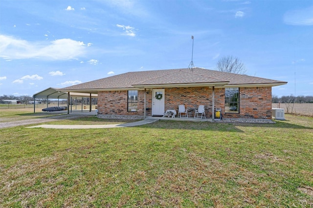 view of front of home featuring brick siding, a shingled roof, central air condition unit, a front yard, and a carport