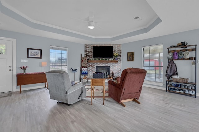 living room with light wood finished floors, visible vents, a brick fireplace, a raised ceiling, and a ceiling fan