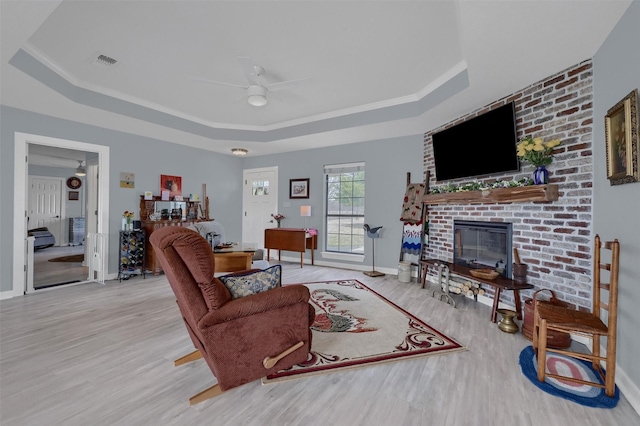 living room featuring a ceiling fan, wood finished floors, visible vents, a tray ceiling, and a fireplace