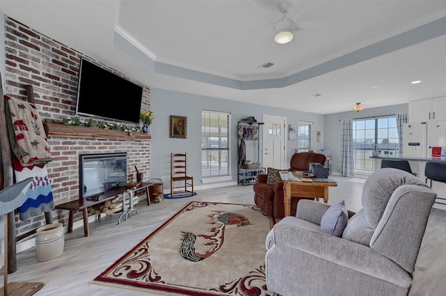 living room with visible vents, a fireplace, light wood-type flooring, and a tray ceiling