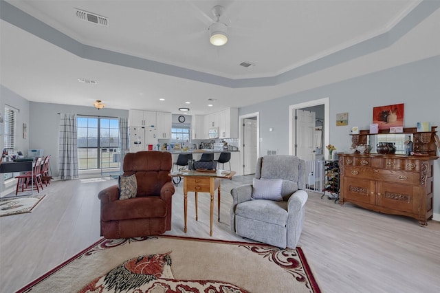 living room featuring visible vents, a raised ceiling, and light wood-style floors