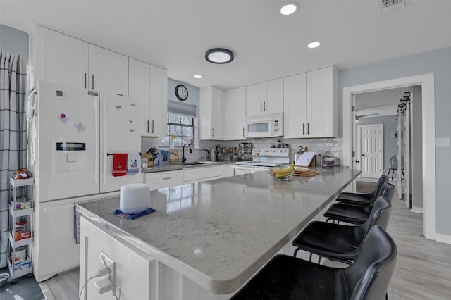 kitchen with white appliances, a breakfast bar, a sink, white cabinets, and tasteful backsplash