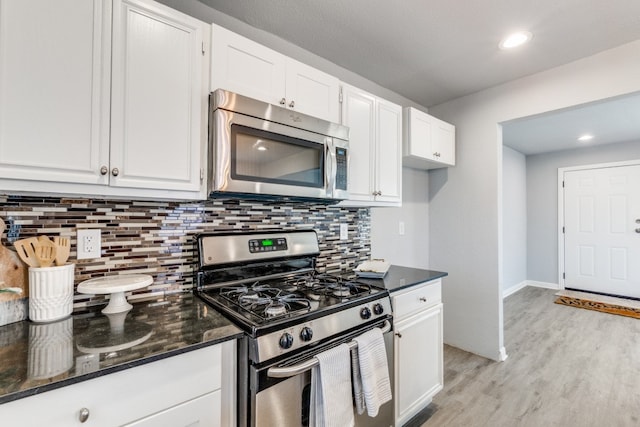 kitchen featuring light wood-type flooring, dark stone countertops, white cabinetry, appliances with stainless steel finishes, and decorative backsplash