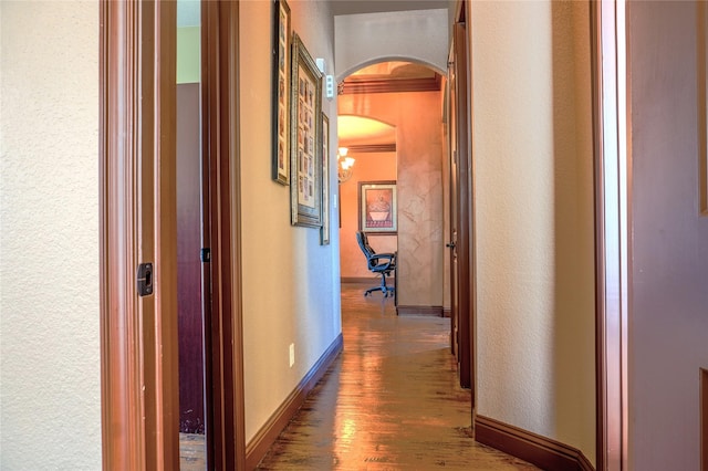 hall with wood finished floors, arched walkways, a textured wall, and baseboards