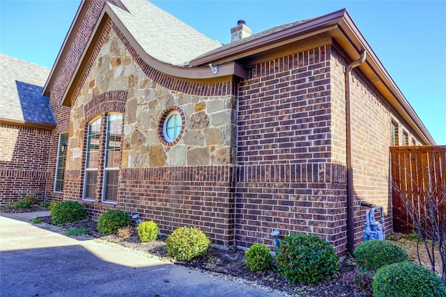 view of property exterior featuring brick siding, stone siding, a chimney, and fence