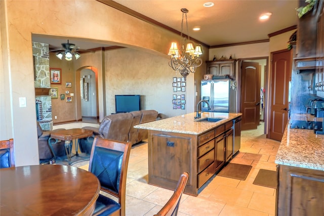 kitchen featuring a sink, arched walkways, stainless steel fridge, crown molding, and light stone countertops