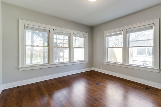 unfurnished room featuring plenty of natural light, baseboards, and dark wood-style flooring