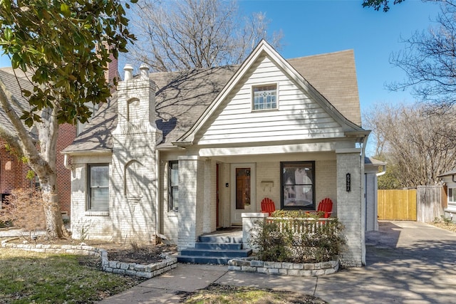 view of front of property featuring brick siding, fence, covered porch, a chimney, and driveway