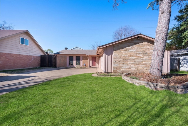 rear view of house featuring fence, concrete driveway, a garage, stone siding, and a lawn