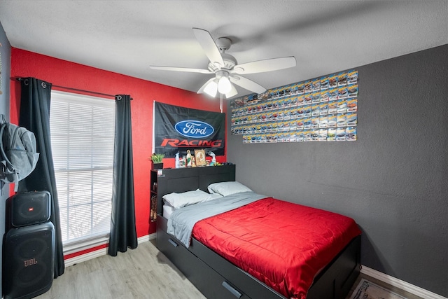 bedroom with a ceiling fan, wood finished floors, baseboards, and a textured wall