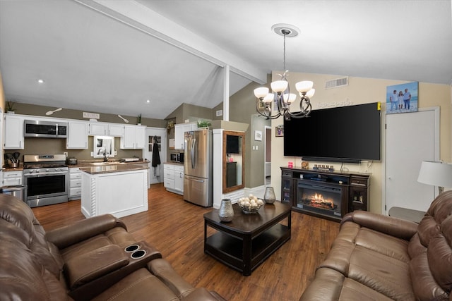 living room with visible vents, a notable chandelier, a warm lit fireplace, dark wood finished floors, and vaulted ceiling with beams