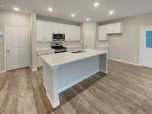 kitchen featuring an island with sink, light wood-style flooring, white cabinets, stainless steel appliances, and a sink