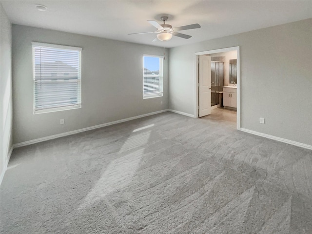 unfurnished bedroom featuring ceiling fan, ensuite bath, baseboards, and light carpet