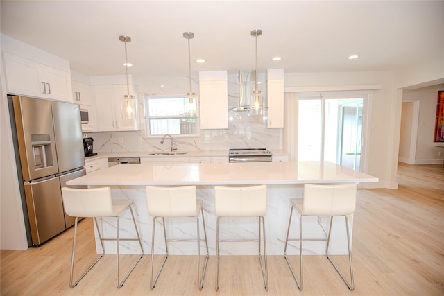 kitchen featuring decorative backsplash, appliances with stainless steel finishes, white cabinets, wall chimney exhaust hood, and a sink