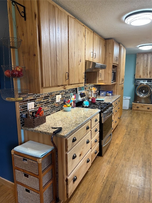 kitchen featuring stainless steel range with gas cooktop, under cabinet range hood, decorative backsplash, light wood-style flooring, and washer / clothes dryer