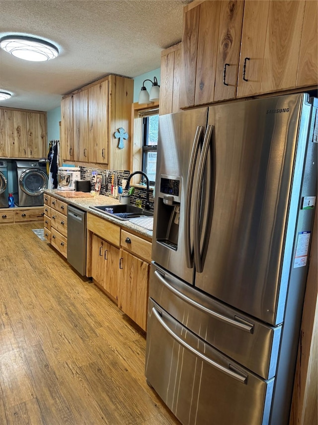 kitchen featuring light countertops, light wood-style flooring, appliances with stainless steel finishes, washer and dryer, and a sink