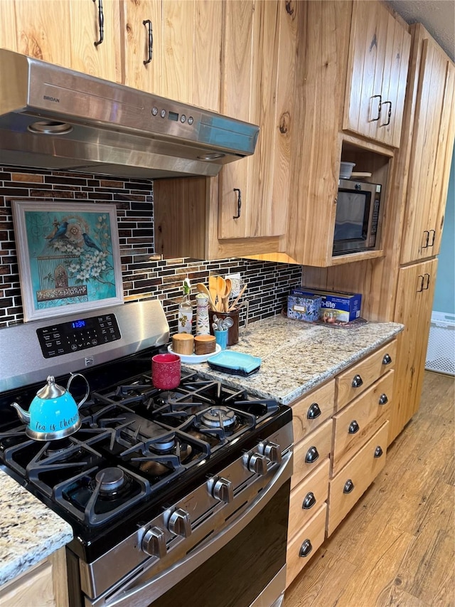 kitchen featuring light wood-style flooring, light brown cabinets, under cabinet range hood, appliances with stainless steel finishes, and decorative backsplash