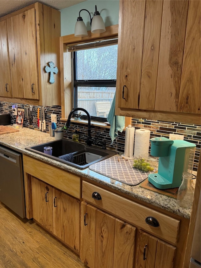 kitchen featuring a sink, decorative backsplash, light wood-style floors, stainless steel dishwasher, and brown cabinets