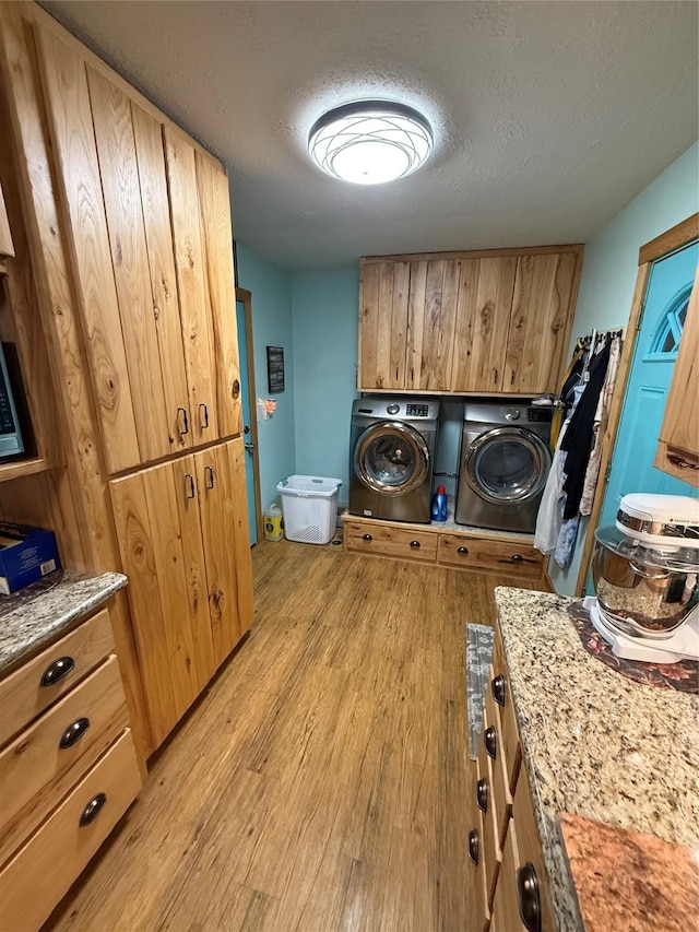 laundry area featuring washing machine and dryer, cabinet space, light wood-style floors, and a textured ceiling