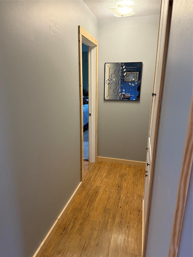 corridor featuring baseboards, a textured ceiling, and wood finished floors