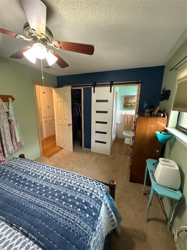 bedroom featuring a ceiling fan, a textured ceiling, a barn door, a closet, and carpet flooring