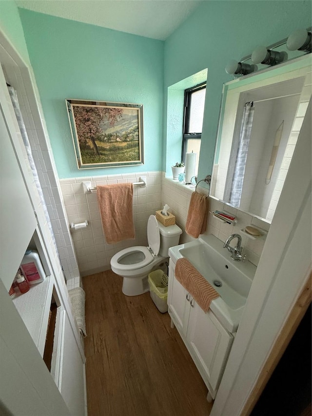 bathroom with tile walls, a wainscoted wall, toilet, wood finished floors, and vanity