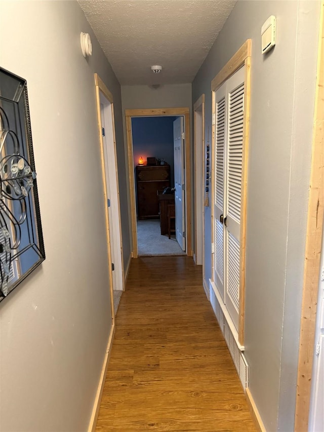 hall featuring light wood finished floors, a textured ceiling, and baseboards