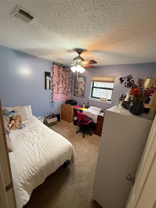 bedroom featuring visible vents, light colored carpet, a textured ceiling, and a ceiling fan