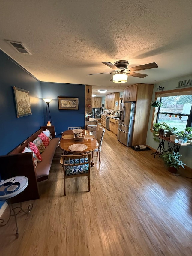 living area featuring visible vents, a textured ceiling, light wood-type flooring, and a ceiling fan