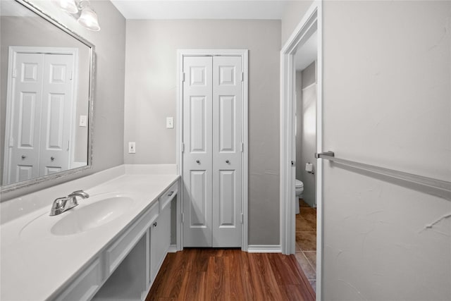 bathroom with a closet, toilet, vanity, and wood finished floors