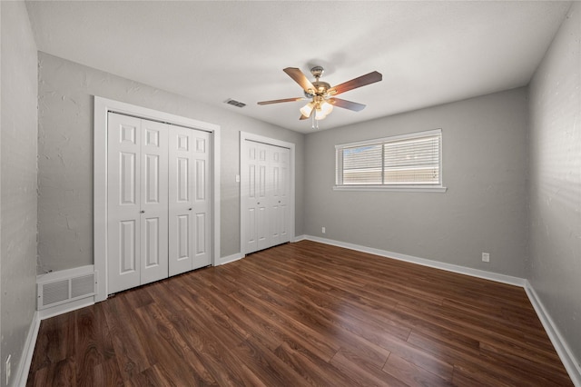 unfurnished bedroom featuring dark wood-style floors, visible vents, two closets, and baseboards