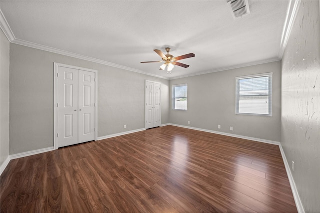 unfurnished bedroom with visible vents, crown molding, multiple closets, and wood finished floors