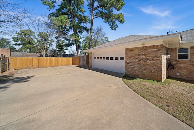 view of side of property featuring a garage, brick siding, driveway, and fence