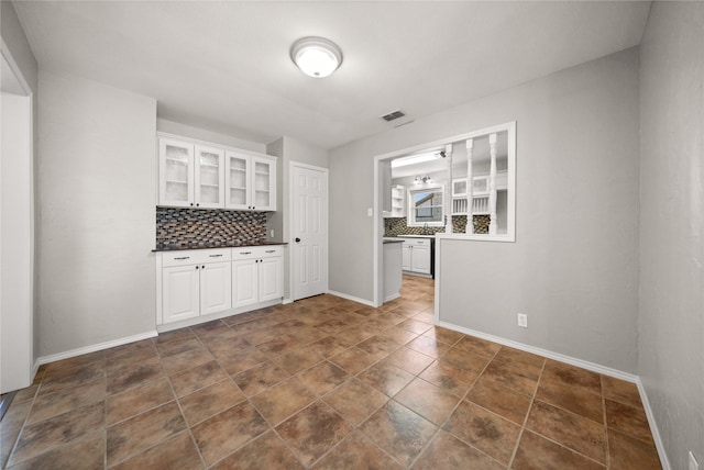 kitchen featuring visible vents, white cabinets, glass insert cabinets, dark countertops, and backsplash