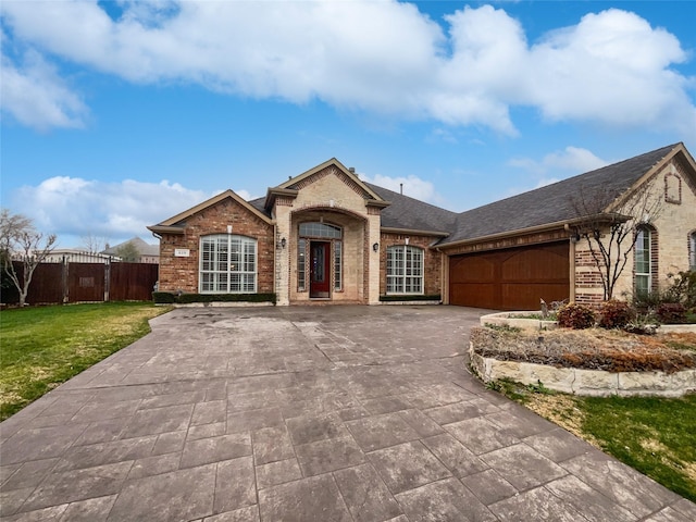 view of front of property featuring brick siding, a front lawn, fence, a garage, and driveway