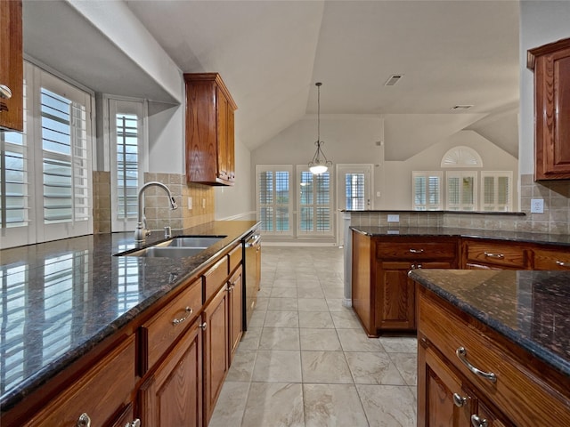 kitchen with a sink, dark stone counters, stainless steel dishwasher, and vaulted ceiling