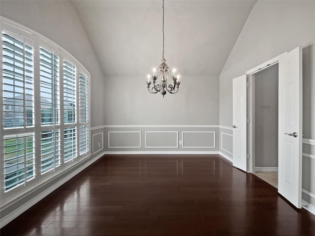 unfurnished dining area with wood finished floors, an inviting chandelier, wainscoting, a decorative wall, and lofted ceiling