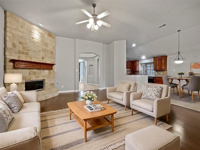 living area with visible vents, a fireplace, light wood-style floors, arched walkways, and a ceiling fan