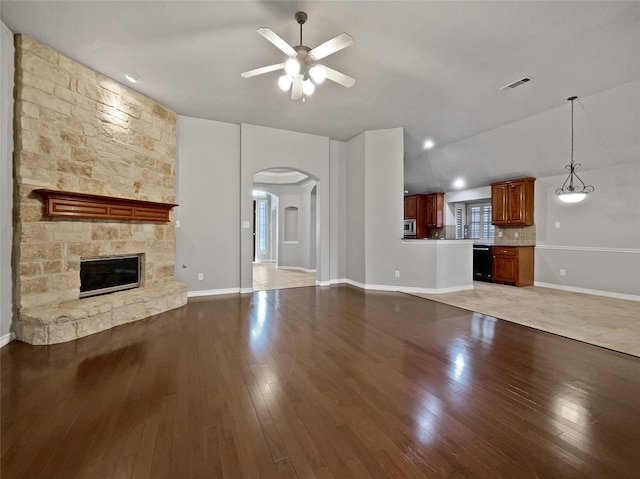 unfurnished living room featuring visible vents, a fireplace, arched walkways, ceiling fan, and light wood-type flooring