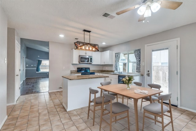 kitchen featuring stainless steel microwave, visible vents, a kitchen island, stove, and white cabinets